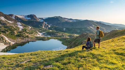 Two people hiking overlooking an alpine lake in the rocky mountains