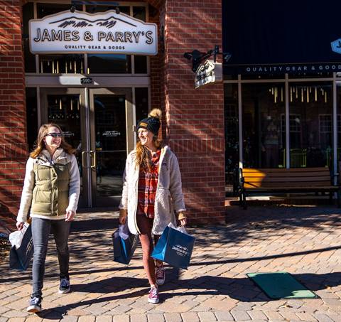 Two women walk out of James & Parry's retail center at Winter Park Colorado Ski Resort with shopping bags