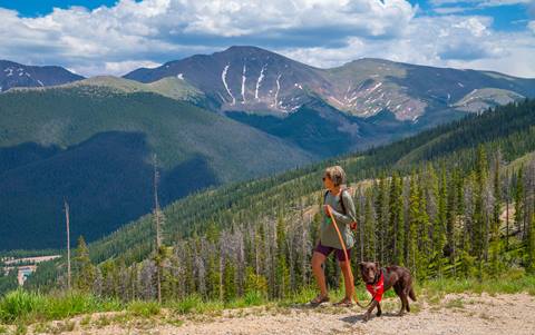 Women walking dog on trail with mountains in the background