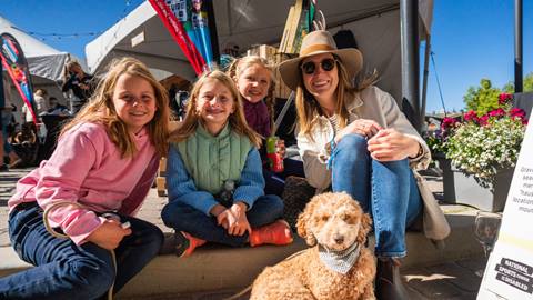 Woman with 3 daughters sitting on ground with dog in the sun at Winter Park Resort