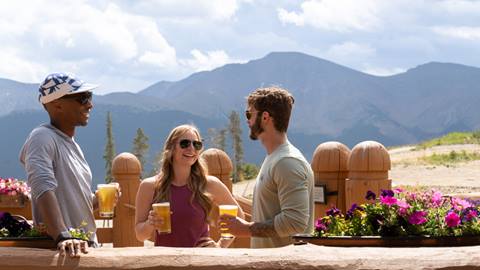 Group of adults drinking beer on a patio overlooking mountains at Winter Park Resort