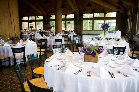 Indoor Wedding reception venue, multiple tables set with white linens and purple and green flowers on each