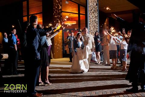 Married couple leaving reception with guest holding sparklers at night at Winter Park Resort. 