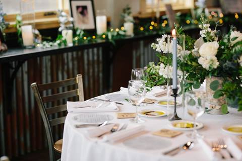 Wedding table set with white linens, candles, and white flowers with greenery. 