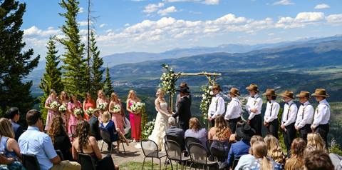 Wedding Ceremony on a mountaintop with guests watching and the rocky mountains in the background at Winter Park Resort.