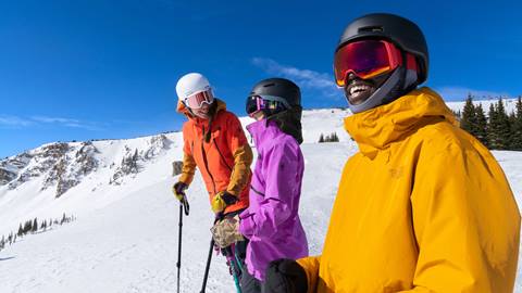 3 Skiers in colorful jackets at the top of a mountain at Winter Park Resort on a bluebird day