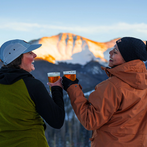 Two friends cheers their drinks as they watch the sunset over Parry Peak at Winter Park Colorado, one of Colorado's best ski resorts.